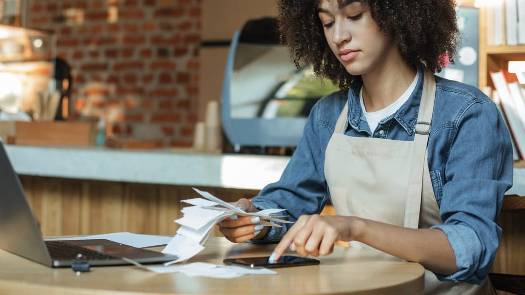 Gerente de restaurante revisando facturas y calculando los costes del negocio con un ordenador y una calculadora.