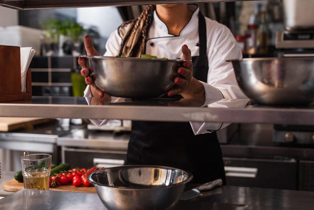 Ayudante de cocina preparando ingredientes en un bol en una cocina profesional.