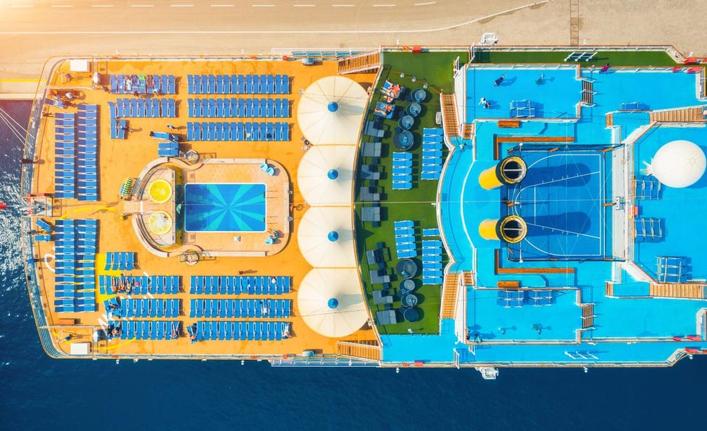 Vista aérea de la cubierta de un crucero con piscinas, tumbonas y zonas de ocio.